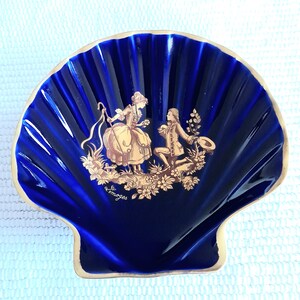 Könnte beinhalten: Eine blaue und goldene Porzellanschale in Muschelform mit einer romantischen Szene eines Paares in Goldfarbe. Die Schale ist mit "Limoges" in goldenen Buchstaben gekennzeichnet.