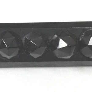 May include: A rectangular, black object with four faceted, gem-like protrusions. The object has a glossy finish and appears to be made of a solid, dark material. The protrusions are evenly spaced.