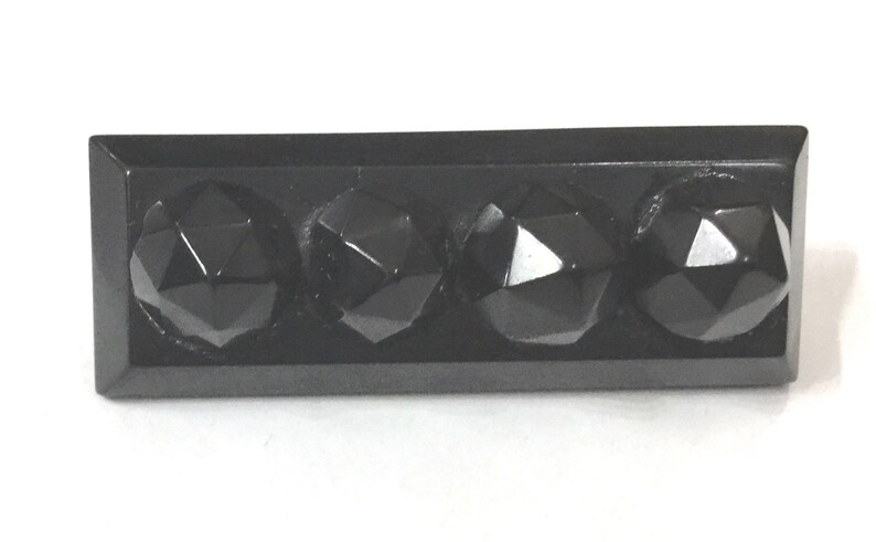 May include: A rectangular, black object with four faceted, gem-like protrusions. The object has a glossy finish and appears to be made of a solid, dark material. The protrusions are evenly spaced.