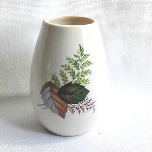 Può includere: Vaso in ceramica color crema con corpo arrotondato e apertura stretta. Il vaso è decorato con un motivo botanico con foglie verdi, marroni e grigie. Le foglie sono disposte a grappolo sulla parte anteriore del vaso.