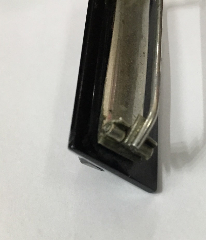 May include: Close-up of a black and silver clipboard clip. The clip has a black frame and a silver metal lever and clasp. The background is white.