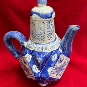 Può includere: Una teiera in ceramica blu e bianca con un design geometrico. La teiera ha un coperchio con un piccolo pomello, un manico curvo e un beccuccio. Il design include motivi floreali e geometrici.