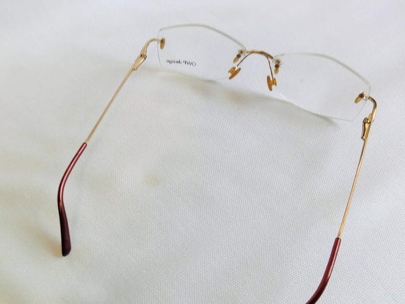 Puede incluir: Gafas sin montura con montura de metal dorado y lentes transparentes. Las patillas tienen un acabado burdeos en los extremos. Las gafas est&aacute;n dise&ntilde;adas con una est&eacute;tica minimalista.
