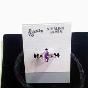 Op de afbeelding: Een sterling zilveren ring met een marquise-geslepen paarse edelsteen. De ring wordt gepresenteerd op een zwarte fluwelen ondergrond met een witte kaart met de tekst "Beau STERLING SILVER". De ring heeft een delicate, open band.