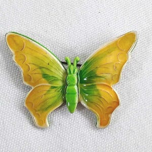 Peut inclure: Broche en forme de papillon avec des ailes jaunes et vertes et un corps vert. La broche présente un design détaillé avec un contour blanc. Les ailes sont un dégradé de jaune à vert. La broche est probablement en émail.