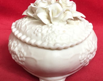 Puede incluir: Caja de porcelana blanca para alhajas con un diseño floral y una tapa decorada con un grupo de rosas blancas.