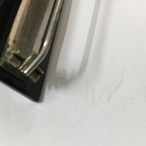 May include: A black clipboard with a silver metal clip. The clipboard is positioned at an angle against a white background. The clip is shiny and reflects light.