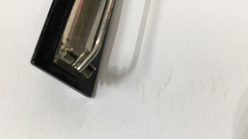 May include: A black clipboard with a silver metal clip. The clipboard is positioned at an angle against a white background. The clip is shiny and reflects light.