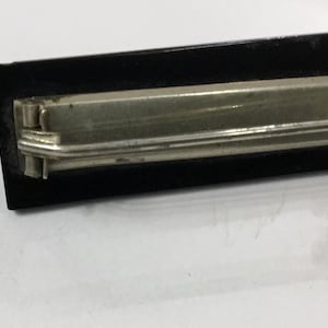 May include: A vintage black and silver metal letter opener. The letter opener has a rectangular black handle and a silver metal blade. The blade is thin and pointed, designed for slicing open envelopes. The opener is likely made of steel.