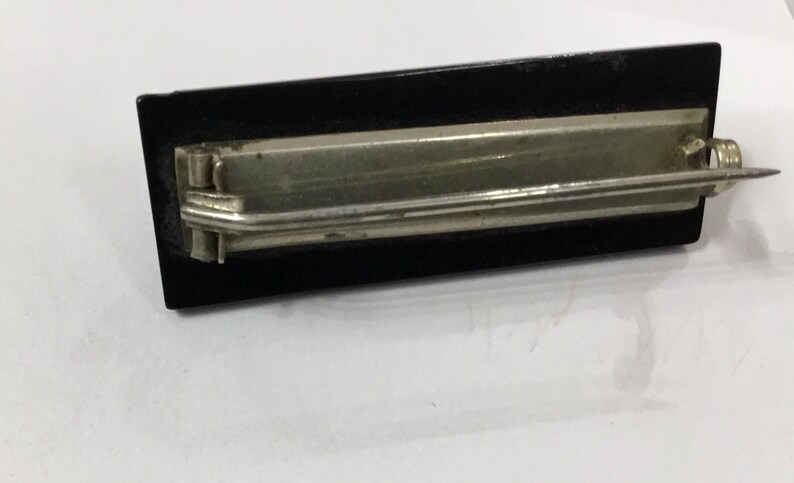 May include: A vintage black and silver metal letter opener. The letter opener has a rectangular black handle and a silver metal blade. The blade is thin and pointed, designed for slicing open envelopes. The opener is likely made of steel.