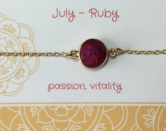 May include: Gold chain bracelet with a round, red ruby gemstone. The card reads "July - Ruby" and "passion, vitality".