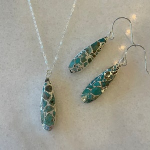 May include: A silver chain necklace and matching earrings with teardrop-shaped turquoise and silver pendants.