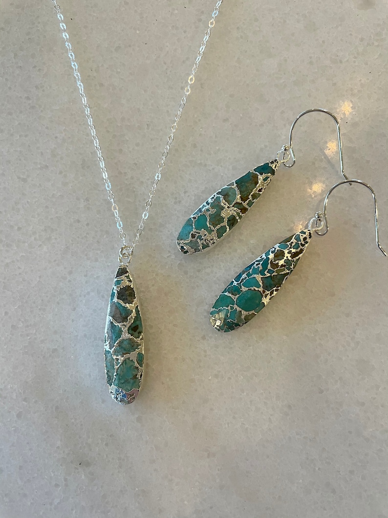 May include: A silver chain necklace and matching earrings with teardrop-shaped turquoise and silver pendants.