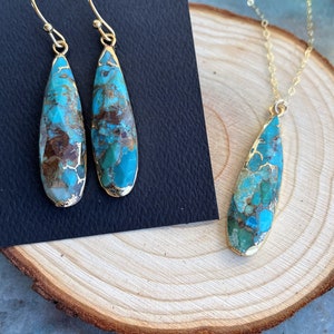 May include: A turquoise and gold necklace and earrings set. The pendant and earrings are teardrop shaped and feature a turquoise stone with brown and gold accents.