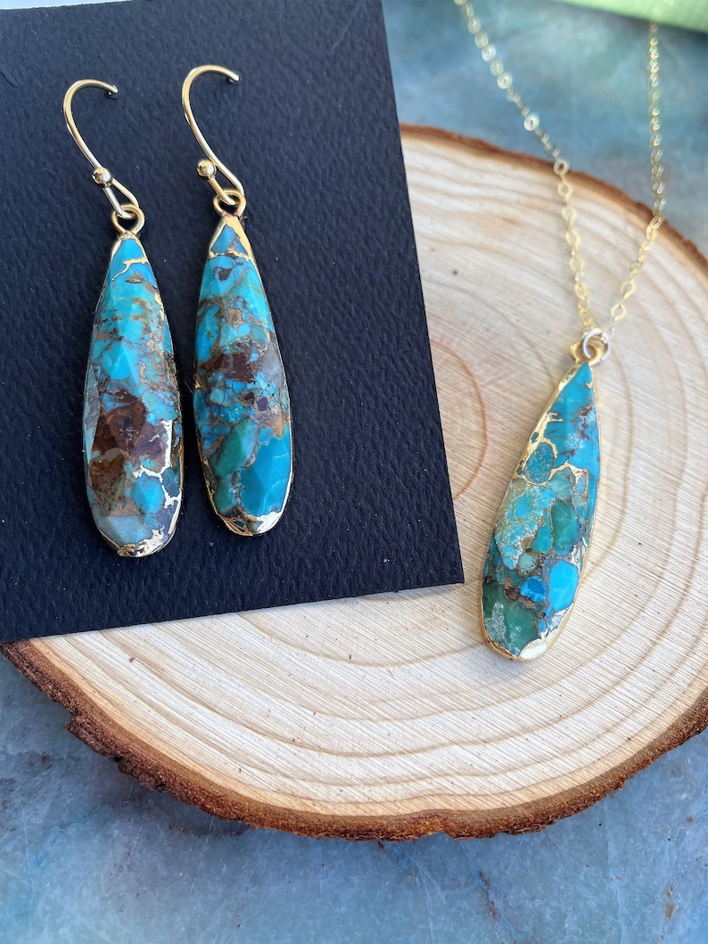 May include: A turquoise and gold necklace and earrings set. The pendant and earrings are teardrop shaped and feature a turquoise stone with brown and gold accents.