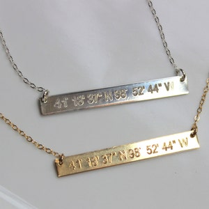 May include: Two gold necklaces with bar pendants engraved with the coordinates "41 18 37 N 98 52' 44" W".