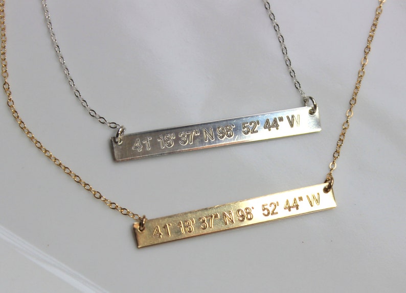 May include: Two gold necklaces with bar pendants engraved with the coordinates "41 18 37 N 98 52' 44" W".