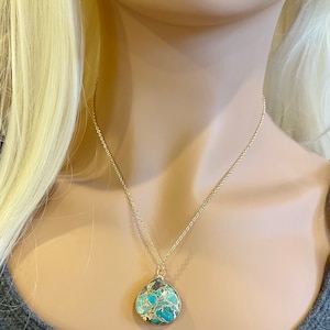 May include: A gold chain necklace with a teardrop-shaped pendant made of turquoise and gold. The pendant has a marbled pattern of blue, green, and gold.