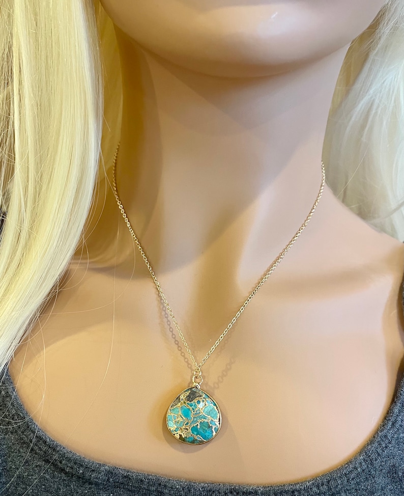May include: A gold chain necklace with a teardrop-shaped pendant made of turquoise and gold. The pendant has a marbled pattern of blue, green, and gold.