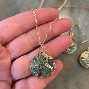 May include: A gold chain necklace with a teardrop-shaped pendant made of turquoise and gold. The pendant has a marbled pattern of blue, green, and brown. The necklace is paired with matching earrings.