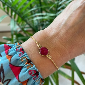 May include: A gold chain bracelet with a single round red gemstone pendant.
