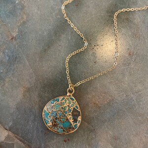 May include: A gold chain necklace with a teardrop-shaped pendant made of turquoise and gold.