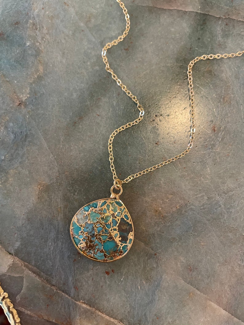 May include: A gold chain necklace with a teardrop-shaped pendant made of turquoise and gold.