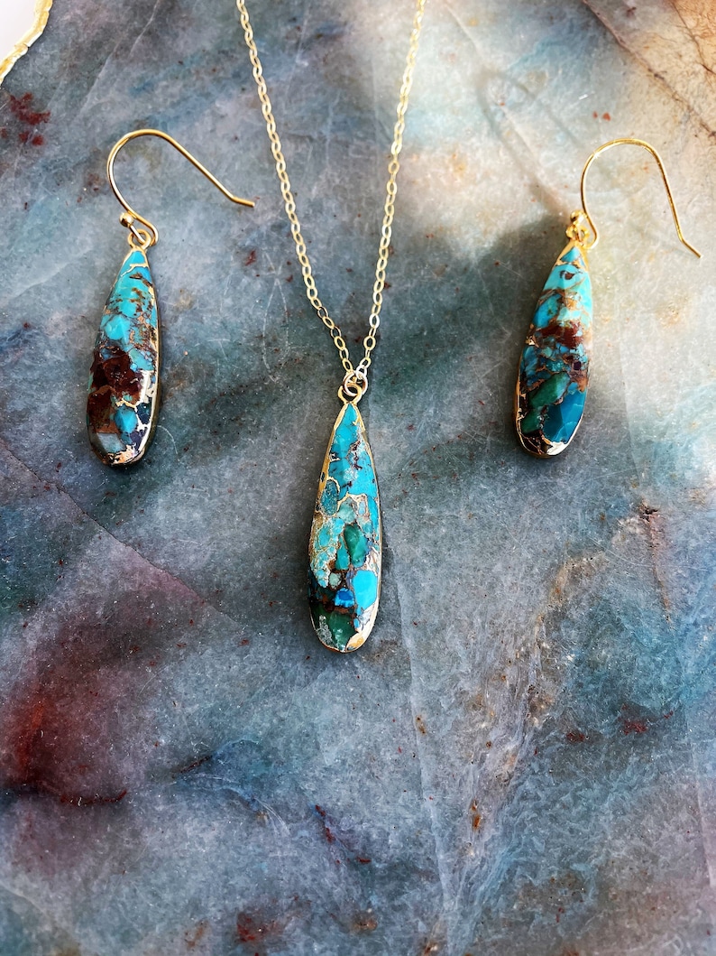 May include: A turquoise and gold teardrop pendant necklace and matching earrings. The pendant and earrings feature a unique, marbled turquoise stone with gold flecks.