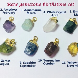 May include: Twelve raw gemstone pendants on gold chains, each representing a different birthstone for the months of the year. The stones are arranged in two rows of six, with the month and stone name labeled below each pendant.