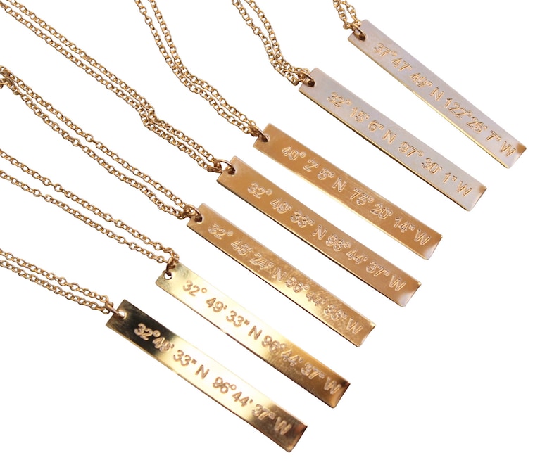 May include: Six gold necklaces with rectangular pendants featuring engraved coordinates. The coordinates are: 37&deg; 47' 68'' N 122&deg; 26' 7'' W, 32&deg; 14' 8&deg; N 37&deg; 30' 1'' W, 40&deg; 25' N 75&deg; 20' 14'' W, 32&deg; 49' 33'' N 96&deg; 44' 37'' W, 32&deg; 46' 24'' N 96&deg; 44' 37'' W, and 32&deg; 49' 33'' N 96&deg; 44' 37'' W.