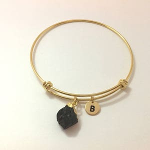 May include: A gold expandable bangle bracelet with a black stone charm and a gold charm with the letter "B" on it.