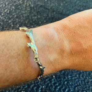 May include: A silver bracelet with a branch design. The bracelet is on a person's wrist.