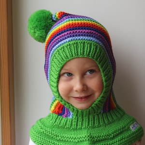May include: A green knitted balaclava with a rainbow striped top and a green pom-pom. The balaclava is made of soft yarn and has a comfortable fit.