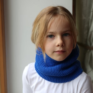 Puede incluir: Una persona joven con una camisa blanca y un cuello de lana azul. El cuello de lana está doblado y es de color azul brillante.