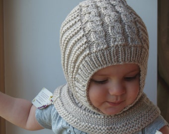 May include: A beige knitted hat with a cable knit pattern covers the head of a child. The hat has a long neck flap that covers the child's neck and shoulders.