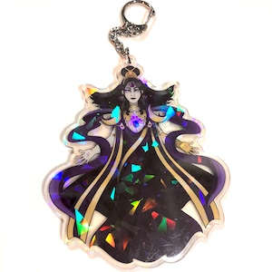 May include: A holographic keychain featuring a woman with long dark hair wearing a purple and gold robe with a jeweled necklace. The background is a glittery iridescent pattern.