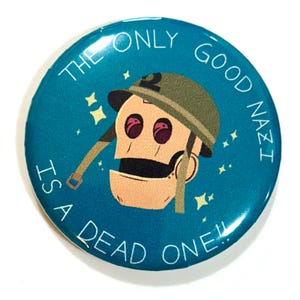 May include: Round teal button with the text "THE ONLY GOOD NAZI IS A DEAD ONE!!" and a cartoon illustration of a robot soldier wearing a helmet. The robot has red eyes and a tan face.