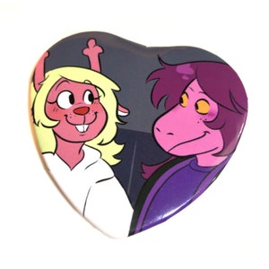 May include: A heart-shaped button featuring a pink and yellow cartoon character with bunny ears and a purple cartoon character with a long snout. The characters are smiling and looking at each other.