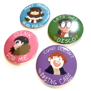 Op de afbeelding: Vier ronde, kleurrijke knoppen met cartoonfiguren en tekst. De knoppen bevatten zinnen zoals "Many Thoughts Head Full", "Let's Get Disco", "Oink For Me" en "Cuno Doesn't %$#&ing Care".