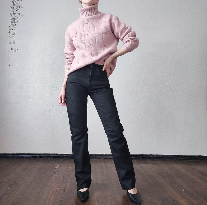 May include: A pale pink cable-knit turtleneck jumper worn with black denim jeans. The jumper features a textured design, and the jeans have a straight leg. Black pointed-toe flats complete the ensemble.
