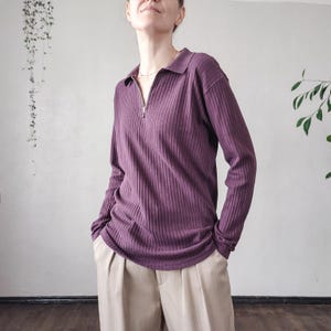 May include: A long-sleeved, plum-colored ribbed knit shirt with a collared neckline and a silver zipper. The shirt is paired with beige pleated pants. The overall style is casual and comfortable.