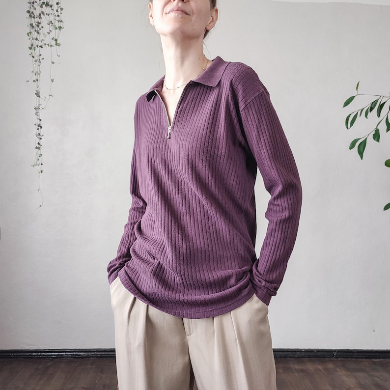 May include: A long-sleeved, plum-colored ribbed knit shirt with a collared neckline and a silver zipper. The shirt is paired with beige pleated pants. The overall style is casual and comfortable.