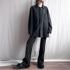 Peut inclure: Une veste utilitaire gris foncé avec une fermeture à boutons et deux grandes poches. La veste est portée sur un pantalon noir à rayures verticales blanches.