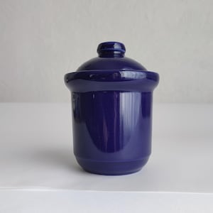 Peut inclure: Un pot en céramique bleu cobalt avec un couvercle assorti. Le pot est de forme cylindrique avec une base arrondie et un bord légèrement évasé. Le couvercle est en forme de dôme avec un petit bouton sur le dessus.