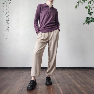 May include: A person wearing a plum-colored, long-sleeved polo shirt with a ribbed texture and a quarter-zip closure. They are wearing beige, wide-leg trousers and black leather loafers. The outfit is styled in a minimalist aesthetic.