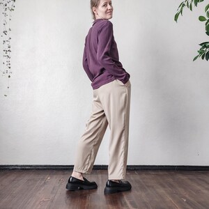 May include: A person wearing a plum-colored ribbed long-sleeve shirt and tan pants. The person is wearing black platform loafers. The outfit is styled in a minimalist aesthetic, with a focus on neutral tones and simple lines.