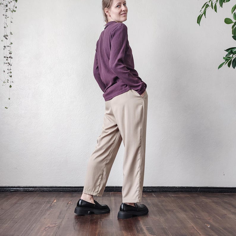 May include: A person wearing a plum-colored ribbed long-sleeve shirt and tan pants. The person is wearing black platform loafers. The outfit is styled in a minimalist aesthetic, with a focus on neutral tones and simple lines.