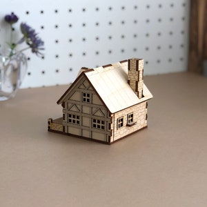 Puede incluir: Un peque&ntilde;o modelo de casa de madera con una chimenea de piedra y ventanas. La casa est&aacute; pintada de color marr&oacute;n claro y tiene un techo blanco.