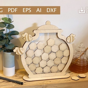 Può includere: Vaso di miele in legno a forma di barattolo con un design a nido d'ape e un coperchio rimovibile. Il vaso è decorato con tre piccole api con facce sorridenti. Il vaso è su una base di legno e ci sono diversi piccoli pezzi di nido d'ape in legno sparsi intorno alla base.