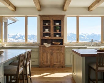 May include: A tall, rustic wooden hutch with glass-paned upper cabinet doors, open shelving, and lower storage cabinets. The hutch features a natural wood grain finish and is positioned between two large windows overlooking snowy mountains.